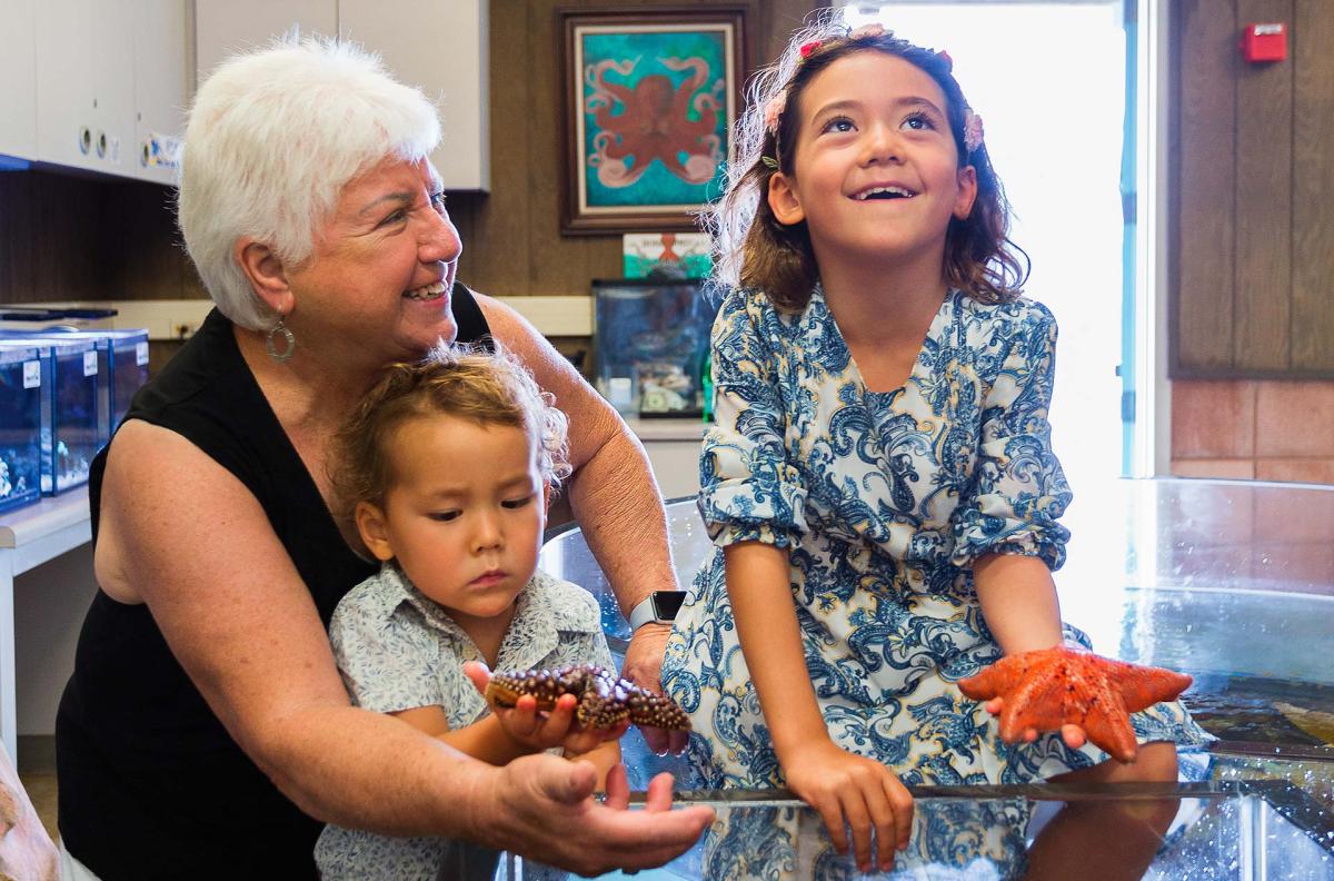 Betty Elings Wells with grandkids holding sea stars at the REEF touch tanks